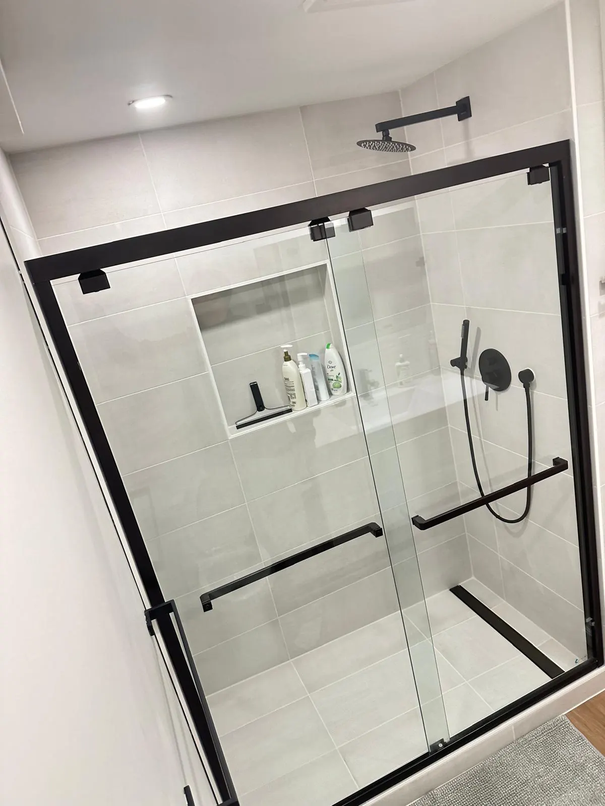 A black-framed sliding shower enclosure, dark fixtures and a recessed wall niche. Bothell, WA