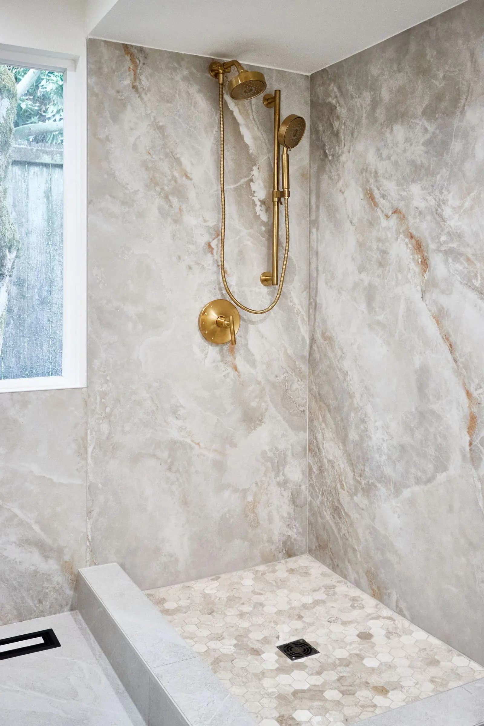 Brass shower fixtures, large-format stone wall tile and a tiled shower floor beneath the window. Bellevue, WA