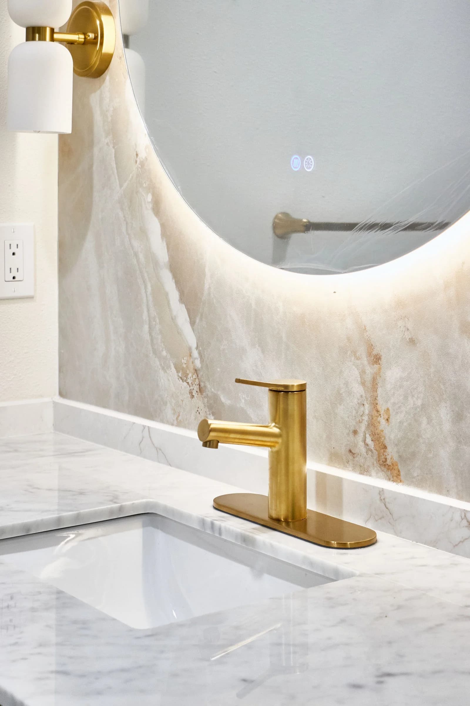 A brass faucet on a white stone vanity top beneath an oval backlit mirror. Bellevue, WA