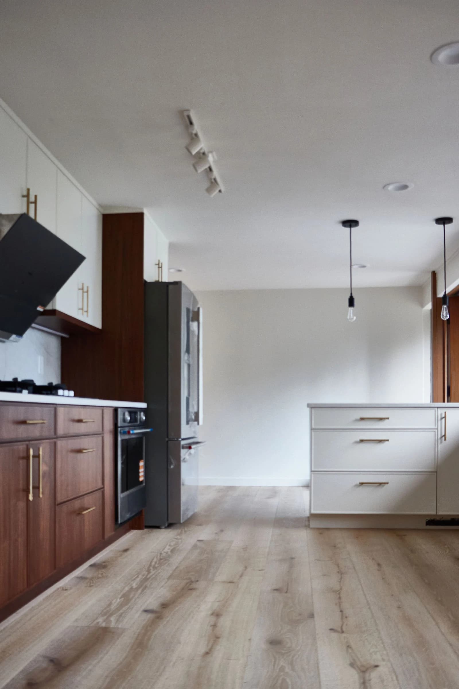 Wood flooring through the kitchen entry, with walnut cabinetry and white counters alongside. Bellevue, WA