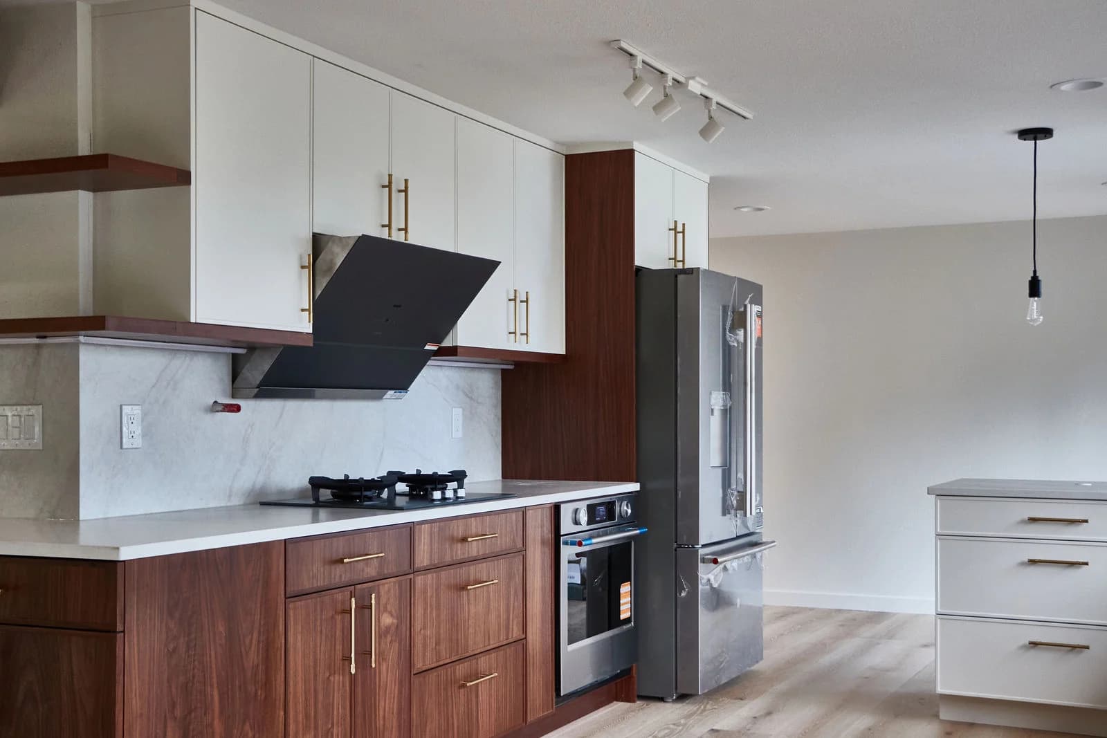 A gas cooktop and angled black hood above white counters, with walnut cabinetry and brass pulls. Bellevue, WA