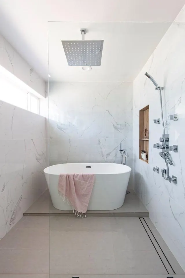 A freestanding tub, overhead shower and veined wall surfaces within a glass enclosure. Bothell, WA