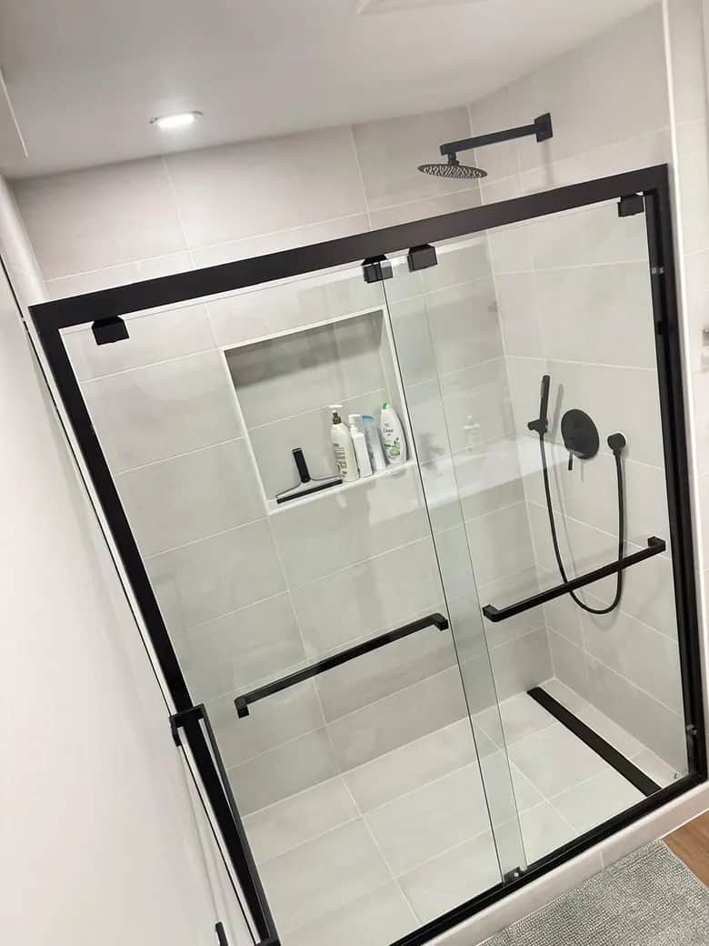 A black-framed sliding shower enclosure, dark fixtures and a recessed wall niche. Bothell, WA