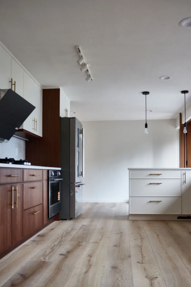 Wood flooring through the kitchen entry, with walnut cabinetry and white counters alongside. Bellevue, WA
