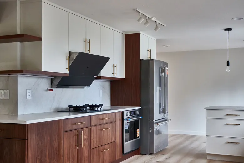 A gas cooktop and angled black hood above white counters, with walnut cabinetry and brass pulls. Bellevue, WA